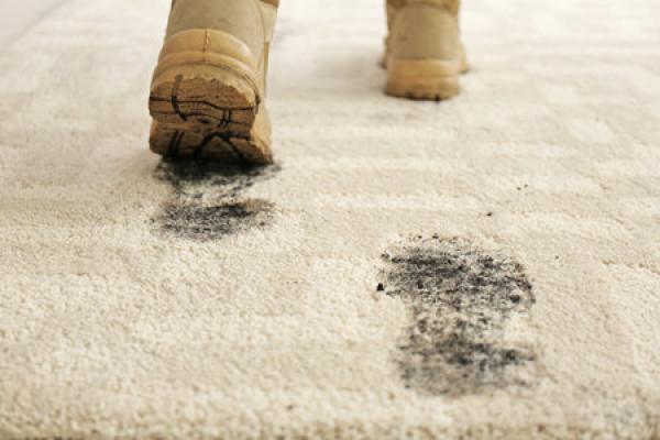 A person in dirty boots walks through a white carpet, leaving dirty footprints